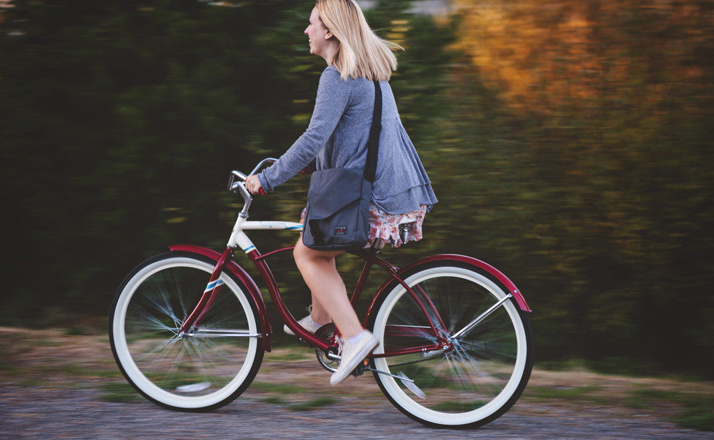 A person wearing the Medium Cafe Bag as a crossbody while riding a bike.