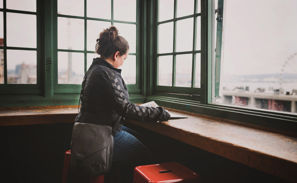 A person wearing a Medium Cafe Bag while reading a book at Pike Place Market.