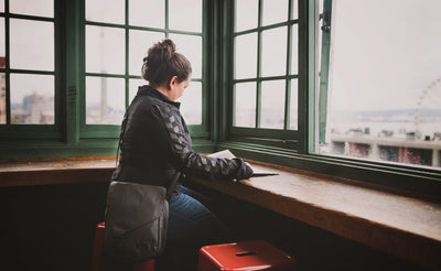 A person wearing a Medium Cafe Bag while reading a book at Pike Place Market.