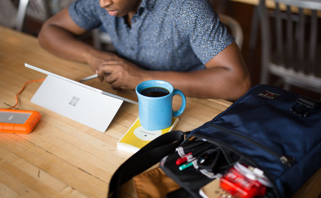 A person working at a table with their Medium Café Bag besides them.