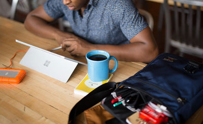 A person working at a table with their Medium Café Bag besides them.