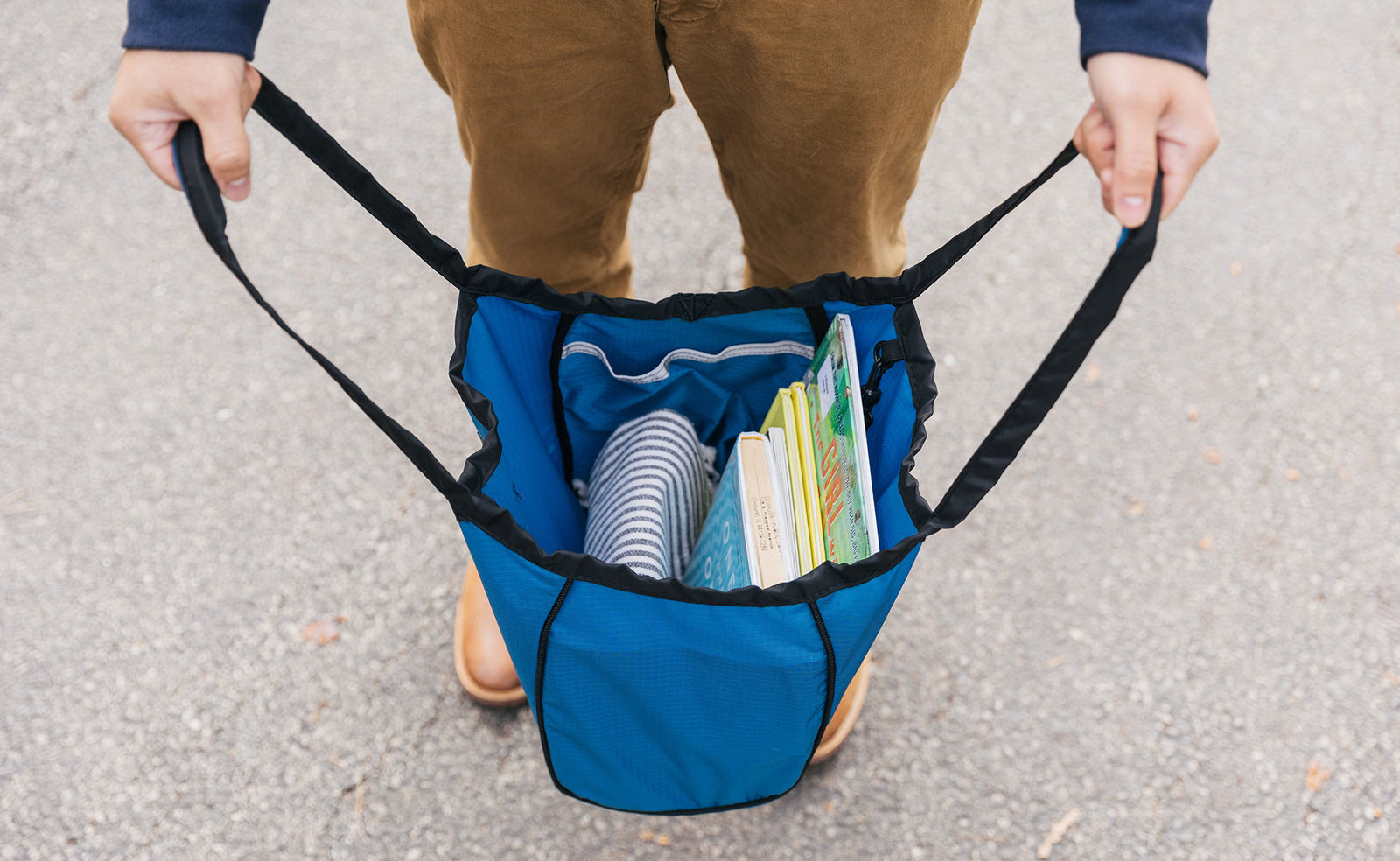 lifestyle visible^^Person holding a Small Original Shop Bag in Cobalt Cerylon open wide. There are books and a blanket inside.