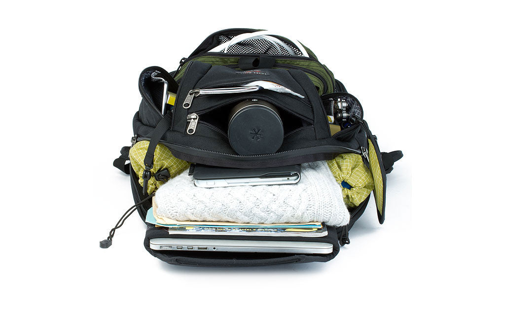 detail visible^^A Synapse 25 with its pockets open, containing a laptop, kitting gear, a water bottle, cables, a multitool, and a wallet.