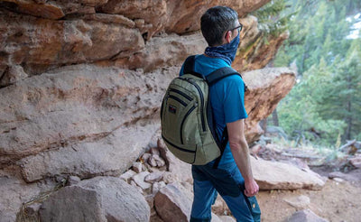 Person standing looking at the view on a hike. They are wearing the Synapse 25 in Taiga.