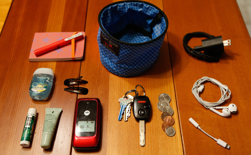 visible detail^^A Small Travel Tray surrounded by various accoutrements, a charge cable, earbuds, a dongle, a bit of change, a pair of keys, a notepad and pen, lotion, chapstick, hair-clips and a flip phone.