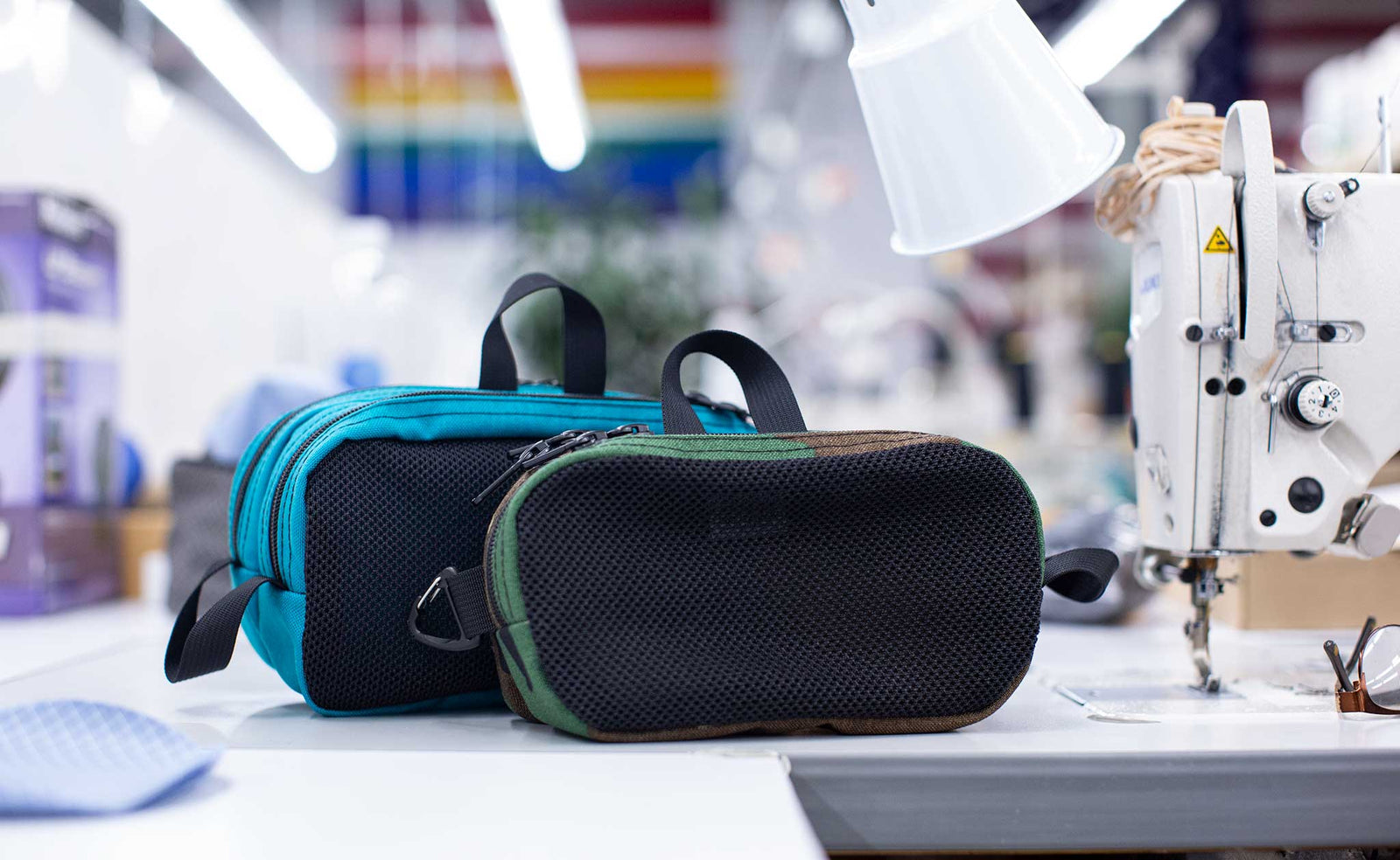 visible lifestyle^^A Large Snake Charmer in Mayura and a Small Snake Charmer in Beaver Camo on a sewing machine table in the TOM BIHN Seattle factory.