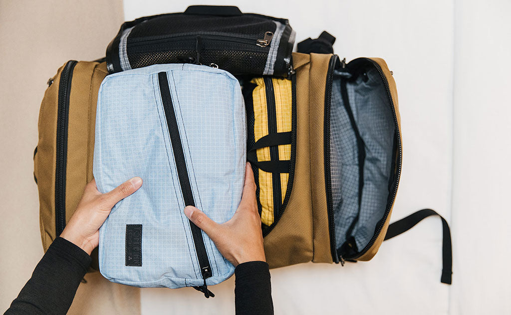 lifestyle visible^^Packing Cube Shoulder Bag in Acuity being packed in an Aeronaut 45 in Coyote.