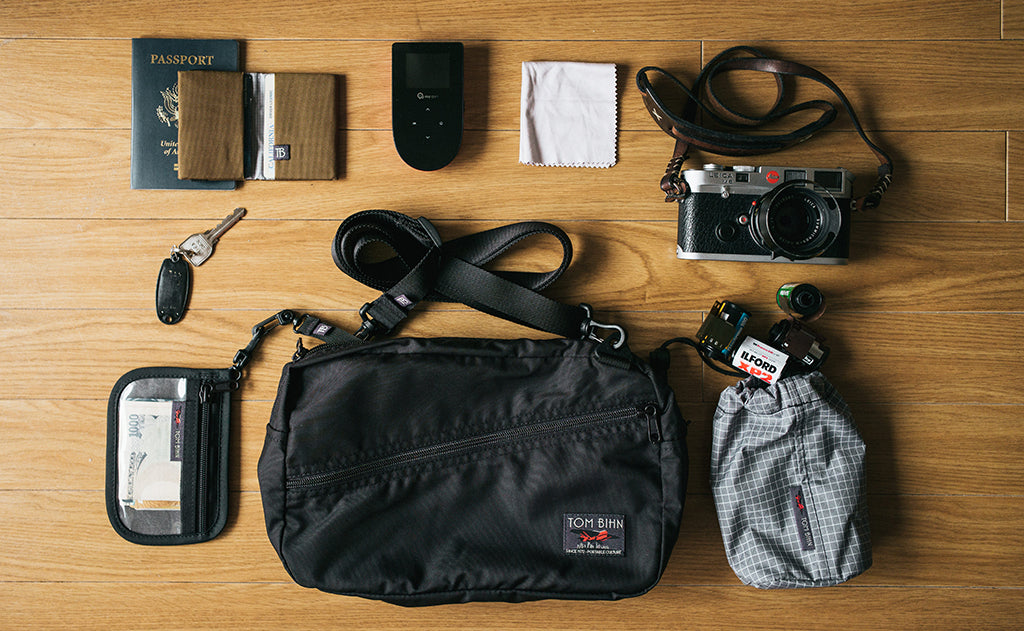 ^^A Packing Cube Shoulder Bag with a possible loadout (a point-and-shoot camera, a clear organizer wallet, a stuff sack with spare batteries, a key fob, a card wallet, a passport, and an MP3 player).