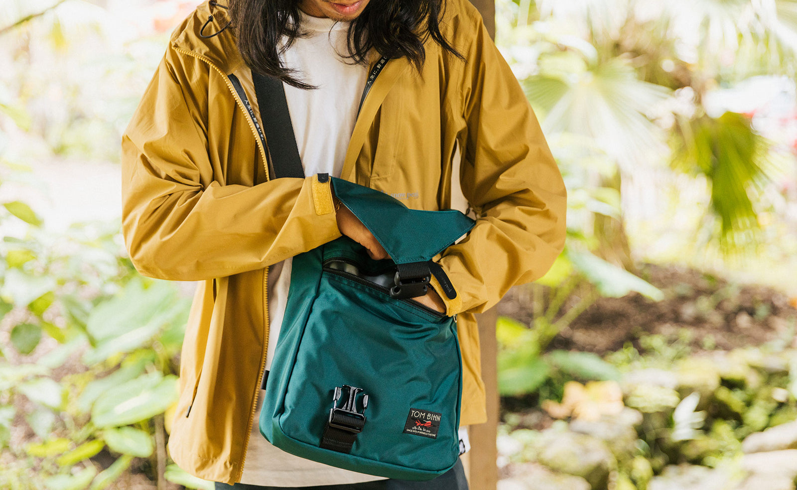 Person wearing the Medium Cafe Bag reaching inside the front zippered pocket.