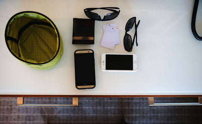^^A Travel Tray set beside a couple of phones, a couple pairs of sunglasses, a couple hotel keys, and a billfold.