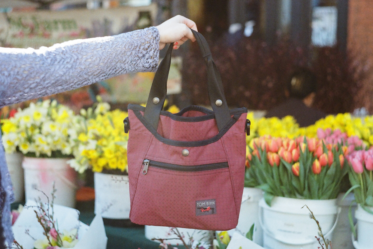 Bordeaux Forager held tote-style over buckets of flowers at a farmers market.