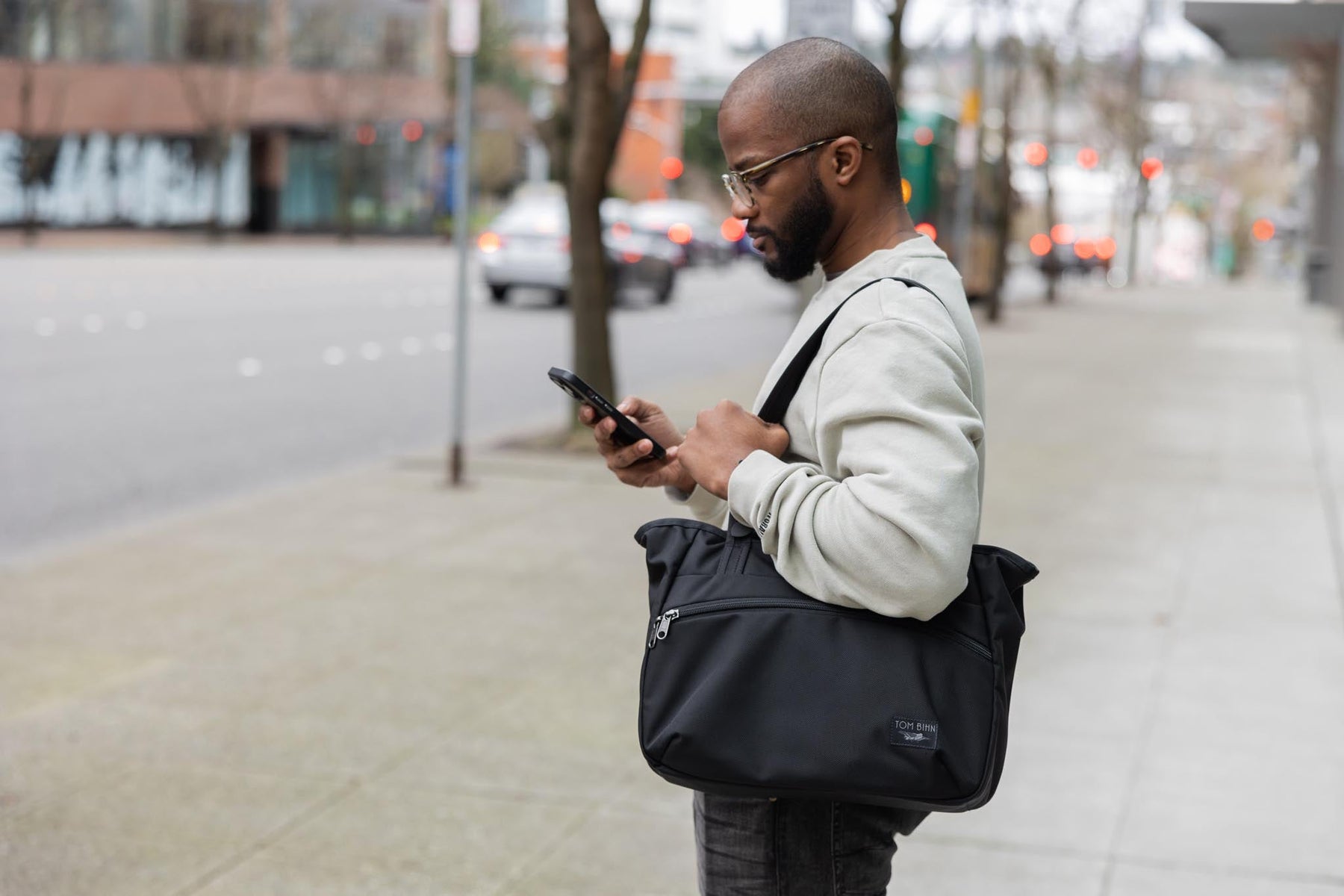 A person standing on the sidewalk wearing the Nomad 11 over their shoulder.