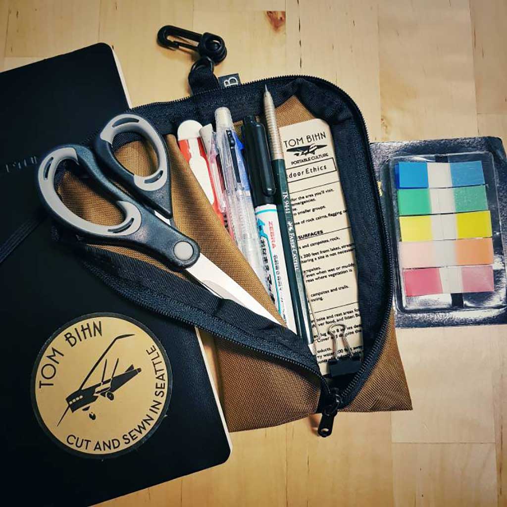 A Coyote Ghost Whale Pouch holding a number of craft supplies such as scissors, pens, and page flags.