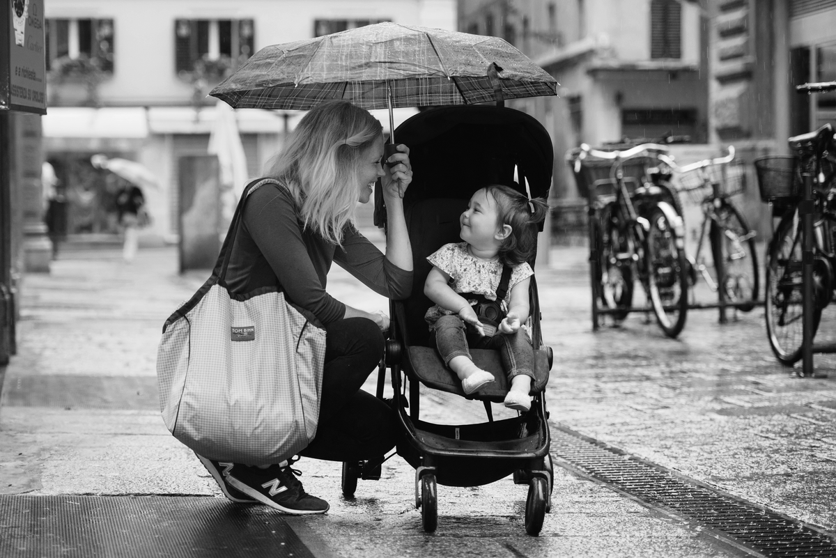 Black and white photo of a woman carrying a Large Zip Top Shop Bag and holding an umbrella over a toddler in a stroller.