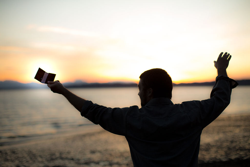 A person on a beach with their arms raised, holding the most minimalist wallet ever made!