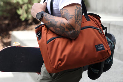 visible lifestyle^^A person carrying the Nomad 16 with the handles, sandals clipped to it and a skateboard in their other hand.