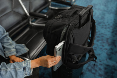 visible lifestyle^^A person removing their laptop from the device pocket of the Bixi while it is on a wheeled bag using its built-in handle passthrough.