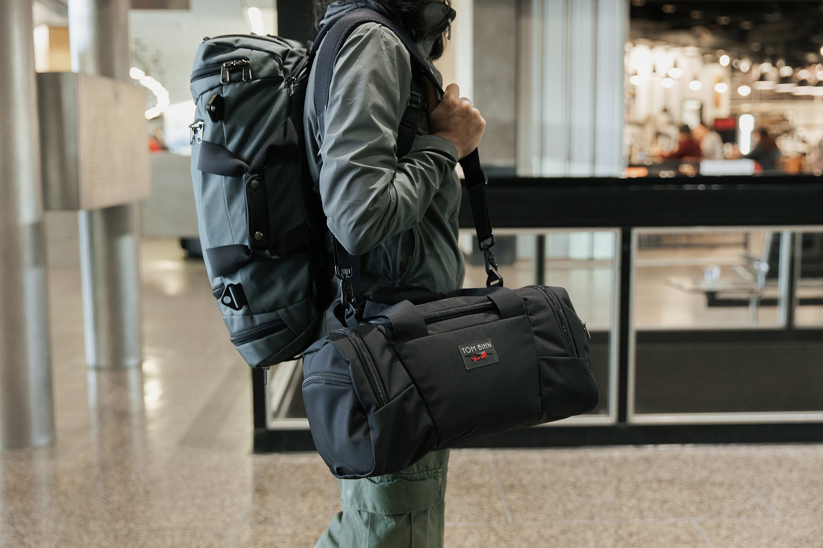visible lifestyle^^Person shoulder carrying the Night Flight Travel Duffel with an Absolute Shoulder Strap and an Aeronaut 45 on their back.