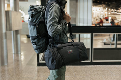 visible lifestyle^^Person shoulder carrying the Night Flight Travel Duffel with an Absolute Shoulder Strap and an Aeronaut 45 on their back.