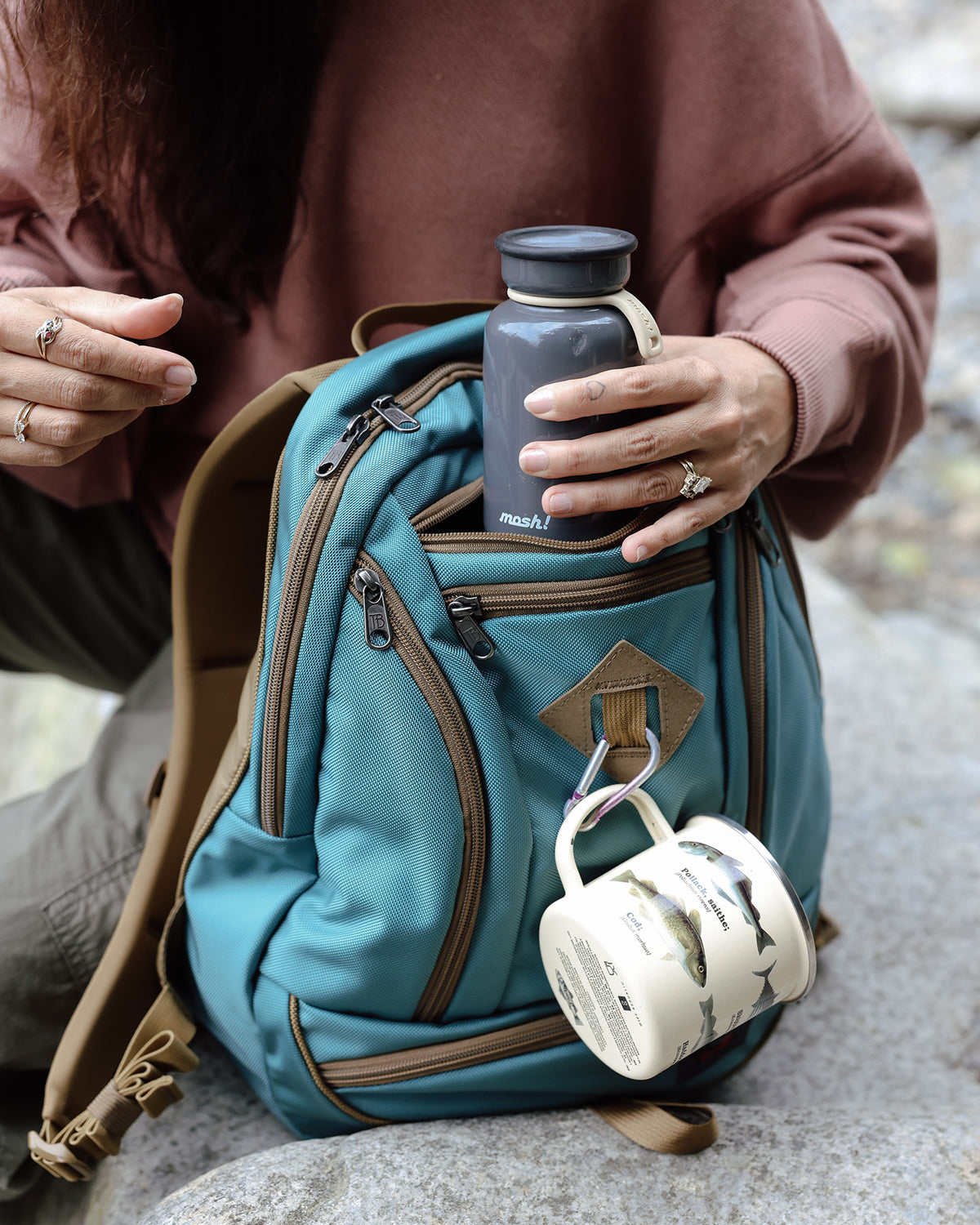 visible lifestyle^^A thermos being pulled from the center pocket of a GE Synapse 19 with a cup hooked on the front attachment point
