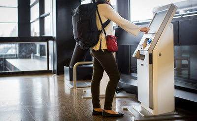 lifestyle visible^^Person wearing an Aeronaut 30 on their back as a backpack and an Everyday Cubelet across their body as they push a button on a check-in kiosk in an airport.