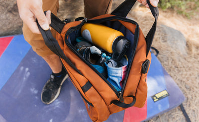 visible detail^^A person holding the Old-School Carry All open: you can see inside of the main compartment and it's packed with a water bottle, chalk bag and other items.