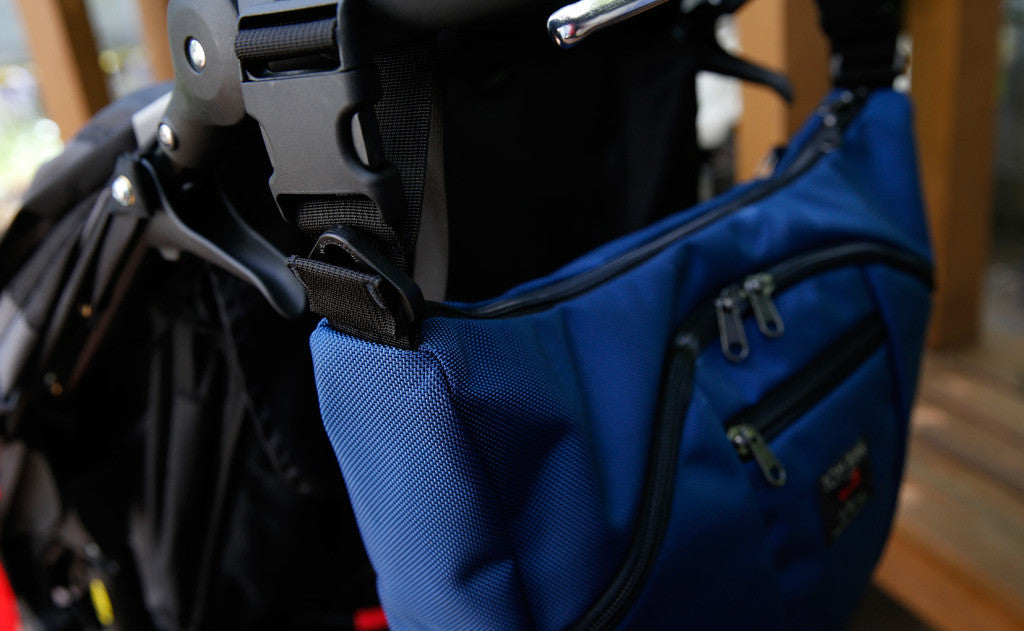 detail visible^^A stroller/wheelchair adapter strap connecting to a Deep Blue (dark blue) 525 Ballistic Parental Unit to the push handle of a stroller.