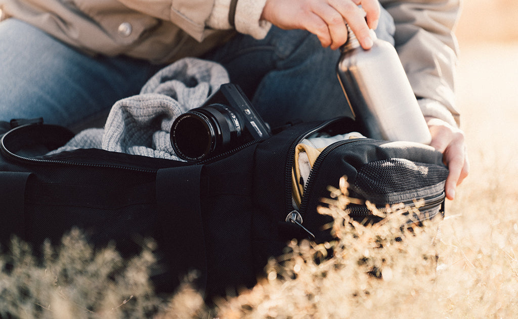lifestyle visible^^A person placing a canteen in the Road Buddy Duffel's end pocket.