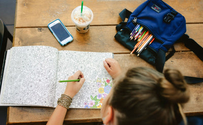 A person with some art supplies in a Small Cafe Book coloring on a coloring book.