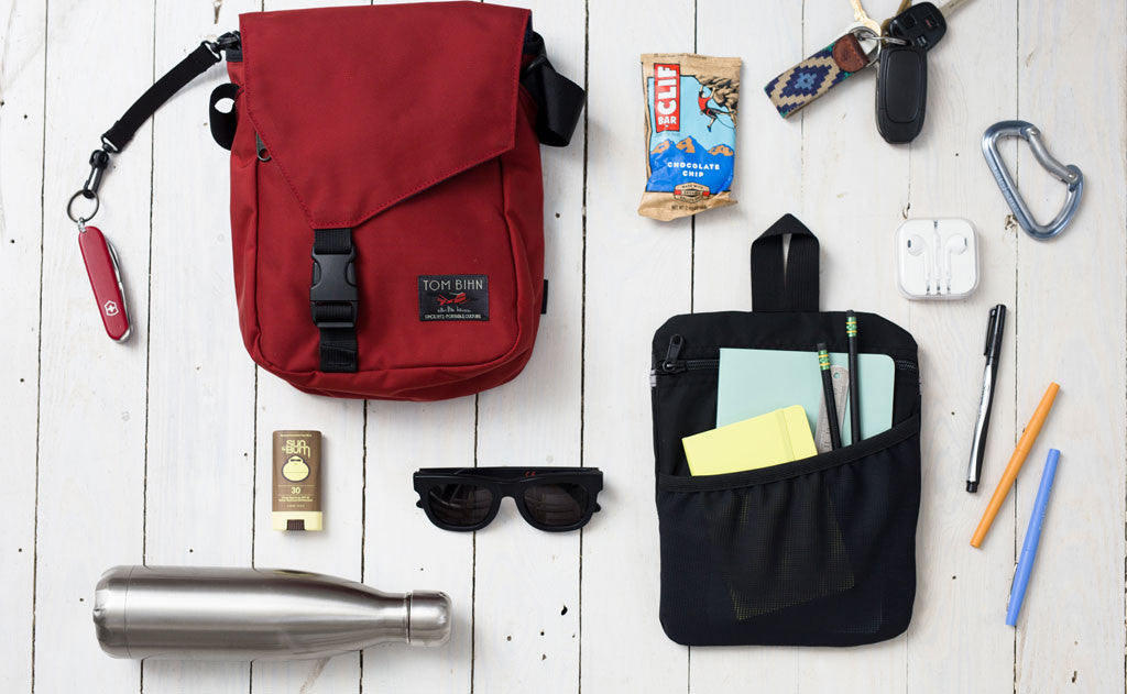 A Small Cafe Bag with some possible items that could fit in it (a small water bottle, writing supplies in a Freudian Slip, a pair of sunglasses, a pocket knife, a protien bar, a pair of keys, a stick of travel deoderant).