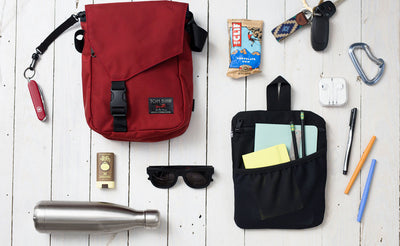A Small Cafe Bag with some possible items that could fit in it (a small water bottle, writing supplies in a Freudian Slip, a pair of sunglasses, a pocket knife, a protien bar, a pair of keys, a stick of travel deoderant).