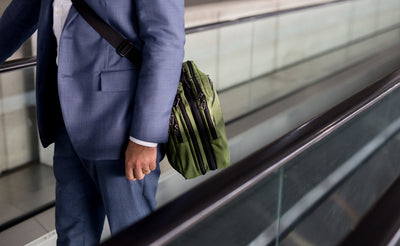 lifestyle visible^^A person on a moving sidewalk carrying The Stowaway via a shoulder strap.