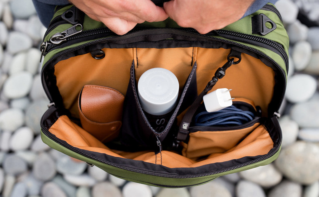 lifestyle visible^^The front main compartment of The Stowaway with the zippered divider zippered holding glasses, a water bottle, and a Cubelet with some charging cables.