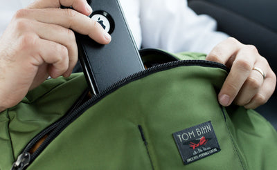 lifestyle visible^^A person retrieving their iPhone from the front zippered-pocket of The Stowaway.