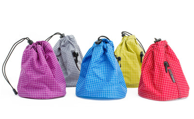 ^^Five Medium Yarn Stuff Sacks in, from left to right, Ultraviolet (purple with white grid) 200 Halcyon, Northwest Sky (light grey with white grid) 200 Halcyon, Island (blue with white grid) 200 Halcyon, Wasabi (green with white grid) 200 Halcyon, and Iberian (red with white grid) 200 Halcyon.