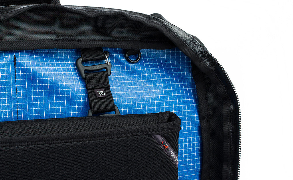 detail visible^^A close shot of the rear main pocket of a Black 525 Ballistic exterior Western Flyer opened to reveal an Island (blue) 200 Halcyon interior with a Cache connected to the nylon loops sewn into the interior seam and a nearby o-ring.