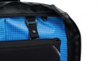 detail visible^^A close shot of the rear main pocket of a Black 525 Ballistic exterior Western Flyer opened to reveal an Island (blue) 200 Halcyon interior with a Cache connected to the nylon loops sewn into the interior seam and a nearby o-ring.