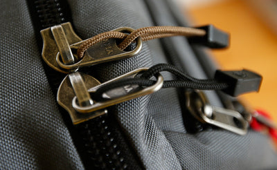 visible variant TB0512A-CA TB0512A-BA^^Cord Zipper Pulls with plastic pull tabs attached to a bag's metal pull tabs.