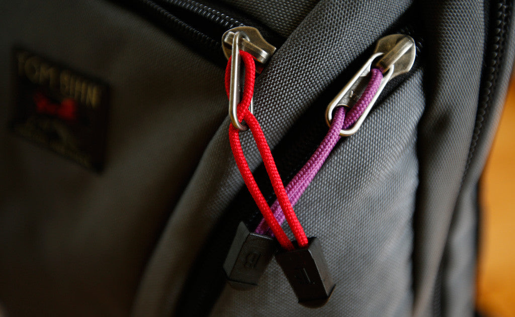 visible variant TB0512A-IA TB0512A-UA^^Cord Zipper Pulls with plastic pull tabs and attached to a bag's metal pull tabs.