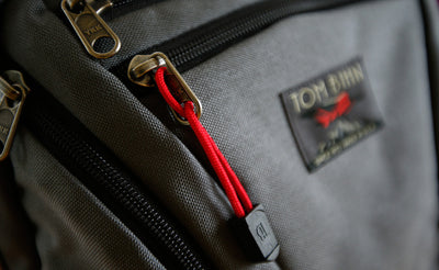 visible variant TB0512A-IA^^Cord Zipper Pulls with plastic pull tabs attached to a bag's metal pull tabs.