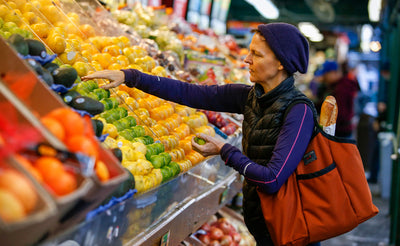 lifestyle visible^^A person with a Moveable Feast over their shoulder picking out some fruit from a fruit stall.