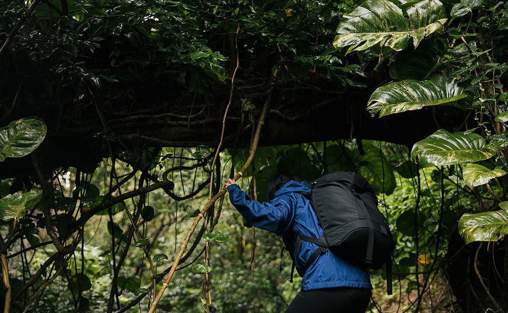 visible lifestyle^^Woman wearing a blue rain coat and the Shadow Guide 33 ducking under a fallen tree on a humid hike in Hawaii.