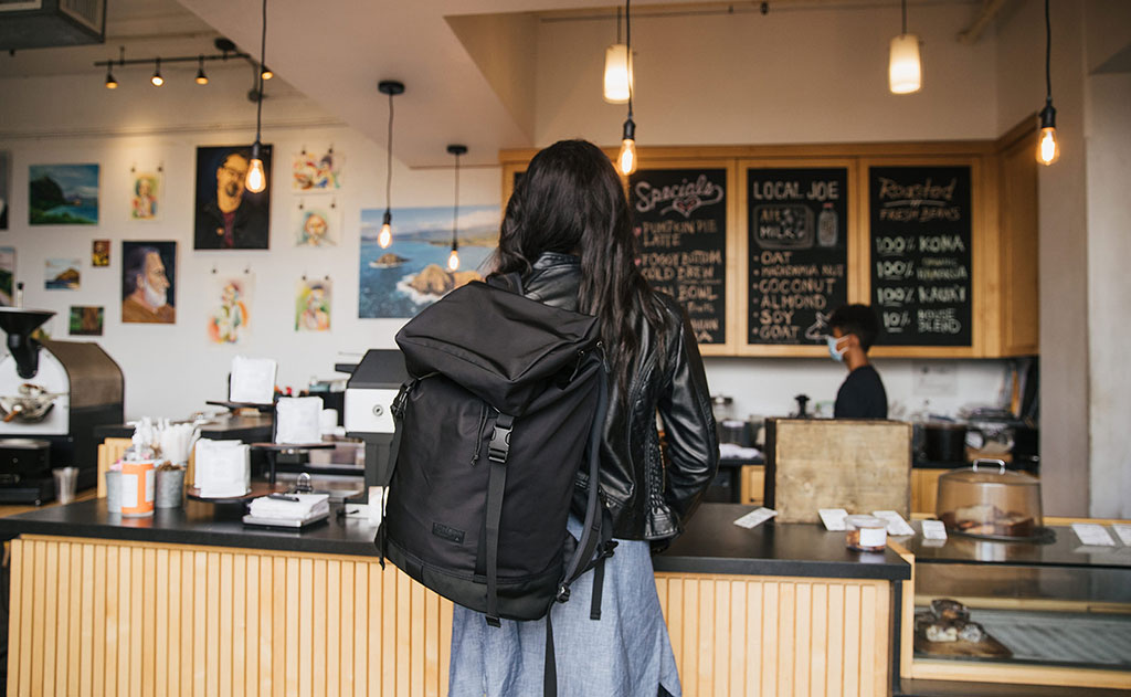 lifestyle visible^^Woman in a coffee shop looking at the menu while wearing the Shadow Guide 33 over one shoulder.