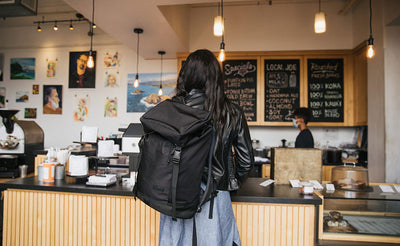 lifestyle visible^^Woman in a coffee shop looking at the menu while wearing the Shadow Guide 33 over one shoulder.