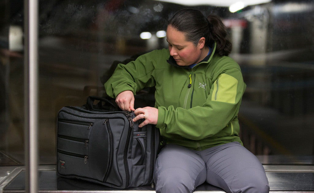 lifestyle visible^^A person seated accessing a main pocket on a Tri-Star while it is next to them on a bench.