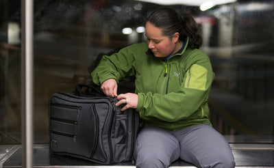 lifestyle visible^^A person seated accessing a main pocket on a Tri-Star while it is next to them on a bench.