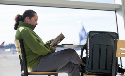 lifestyle visible^^A person reading a book at the airport cafe with a Tri-Star in the seat beside them.