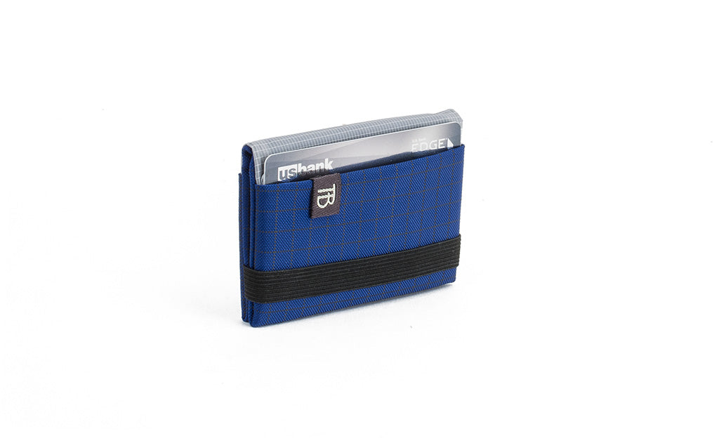 visible variant TB1277-DH^^The Size 1 Nik's Minimalist Wallet in Nordic (blue with grey grid) 400 Halcyon closed pockets-out with the attached elastic band.