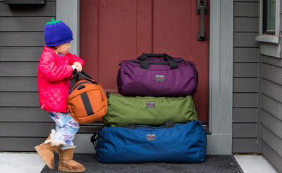 lifestyle visible ^^ A child with the Mini Yeoman Duffel next to a stack of a Small, Medium, and Large Yeoman Duffel.