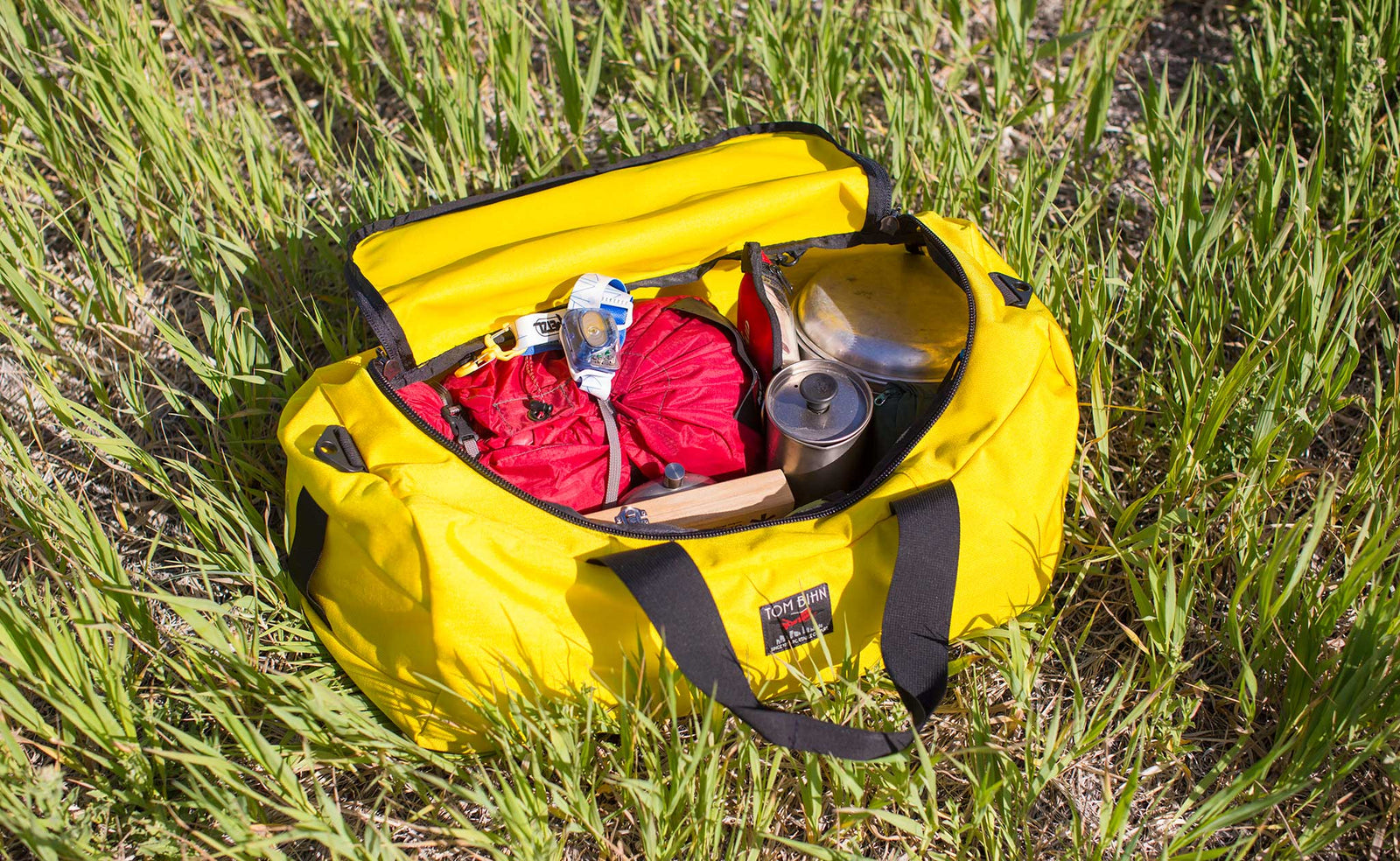 lifestyle  visible^^Canary (yellow) 1000d Cordura Large Yeoman filled with camping gear, laying in the grass.